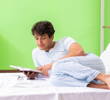 Genç yakışıklı öğrenci yatakta kitap okuyor.