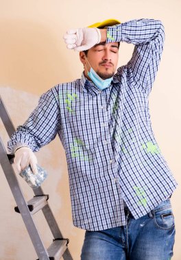 Genç müteahhit zımpara kağıdıyla duvarı zımparalıyor.