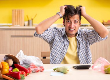 Genç adam mutfakta sebze masraflarını hesaplıyor.