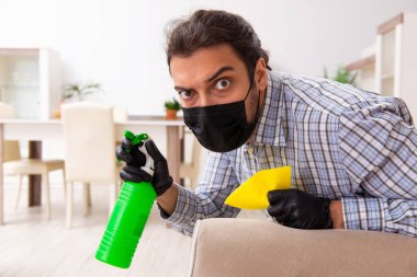 Genç erkek müteahhit Coronavirus konseptiyle evi temizliyor.