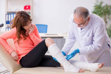 Genç bacak yaralı kadın yaşlı doktor travmatoloğu ziyaret ediyor.