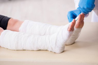 Genç bacak yaralı kadın yaşlı doktor travmatoloğu ziyaret ediyor.