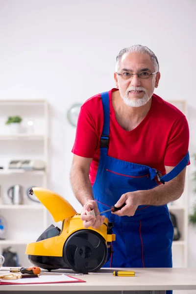 Viejo contratista reparando aspiradora en interiores —  Fotos de Stock