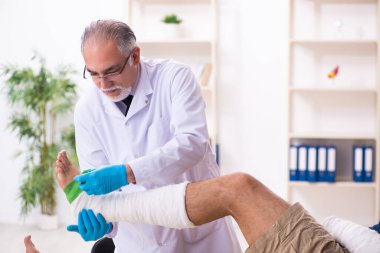 Genç yaralı adam yaşlı doktor travmatoloğu ziyaret ediyor.