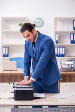 Young male employee making copies at copying machine clipart
