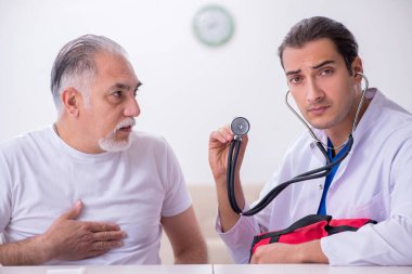 Genç erkek doktor yaşlı erkek hastayı ziyaret ediyor.