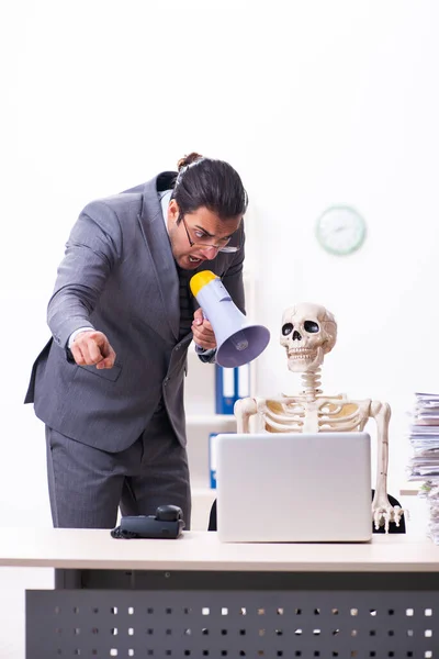 Jonge mannelijke werknemer en skelet in het kantoor — Stockfoto