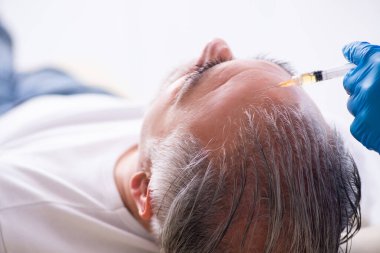 Yaşlı adam saç nakli için genç erkek doktoru ziyaret ediyor.