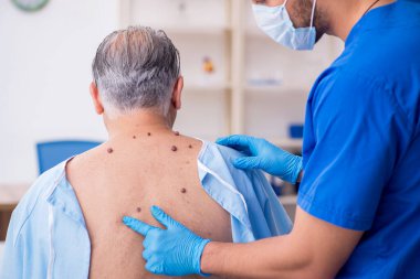 Yaşlı adam genç erkek doktor dermatoloğu ziyaret ediyor.