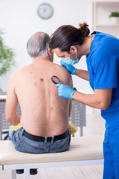 Homem velho visitando jovem médico dermatologista masculino — Fotografia de Stock