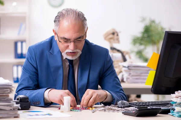 Old male sick employee working overtime in the office