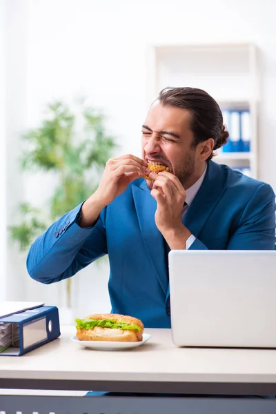 Ung manlig anställd som äter frukost på arbetsplatsen — Stockfoto