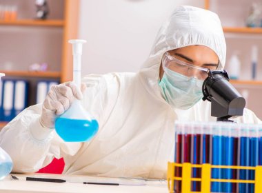 Laboratuvarda çalışan koruyucu elbise giyen genç bir biyokimyacı.