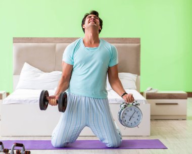 Pijamalı genç adam sabah egzersizi yapıyor.