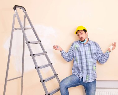 Genç müteahhit zımpara kağıdıyla duvarı zımparalıyor.