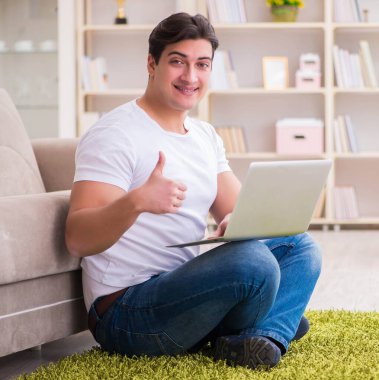 Evde, halı döşemesinde dizüstü bilgisayarda çalışan bir adam.