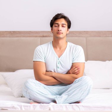 Genç adam yatakta yoga yapıyor.