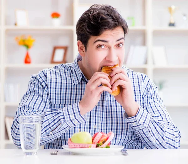 El hombre tiene un dilema entre la comida sana y el pan en la dieta con —  Fotos de Stock