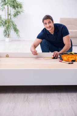 Genç erkek müteahhit eve mobilya kuruyor.