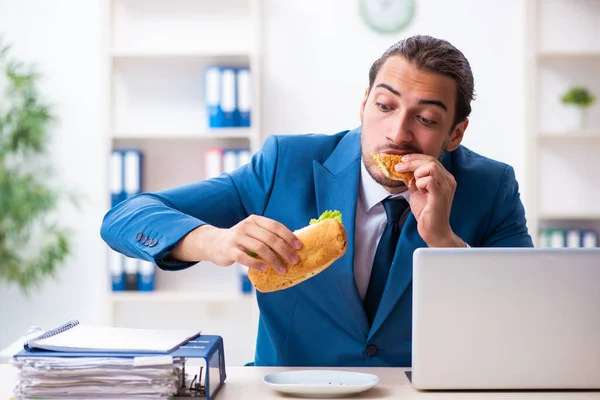 Ung manlig anställd som äter frukost på arbetsplatsen — Stockfoto