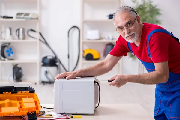 Empreiteiro velho do sexo masculino reparar microondas dentro de casa — Fotografia de Stock