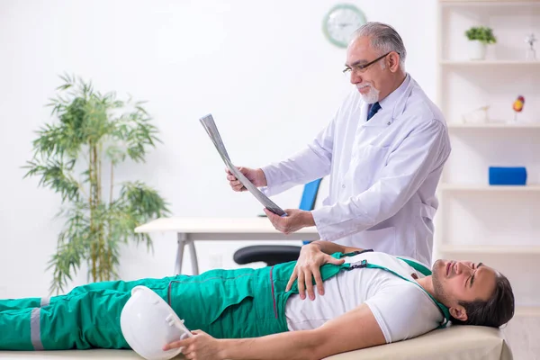 Young male contractor visiting old doctor — Stock Photo, Image