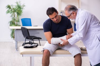 Genç yaralı adam deneyimli erkek doktor travmatologları ziyaret ediyor.