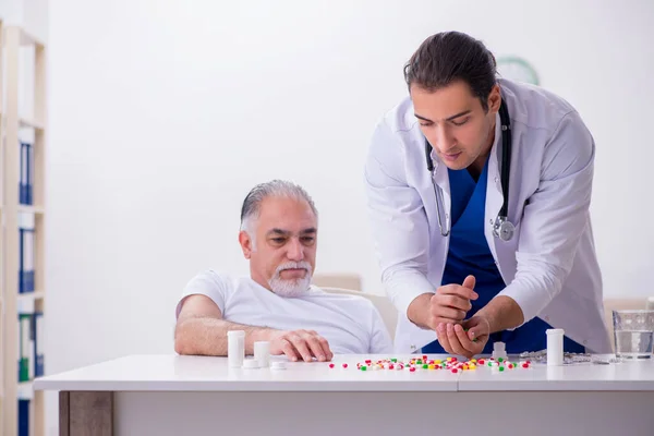 Joven médico masculino visitando a viejo paciente masculino en casa —  Fotos de Stock