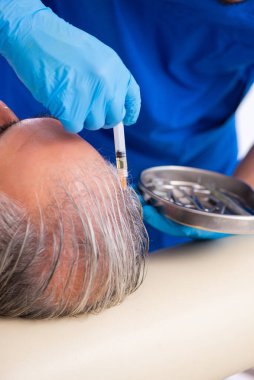 Yaşlı adam saç nakli için genç erkek doktoru ziyaret ediyor.