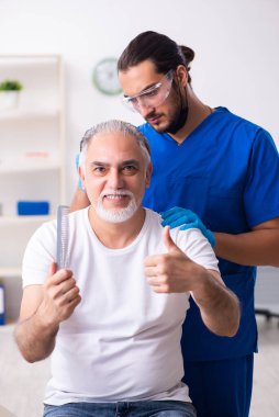 Yaşlı adam saç nakli için genç erkek doktoru ziyaret ediyor.