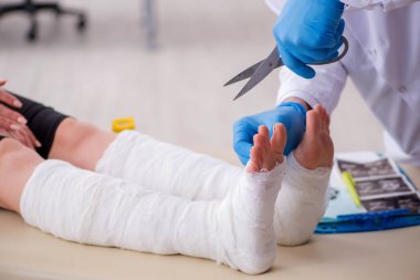 Genç bacak yaralı kadın yaşlı doktor travmatoloğu ziyaret ediyor.