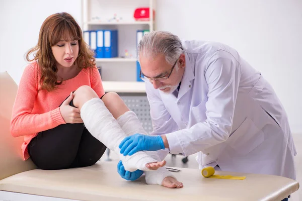Jonge been gewonde vrouw op bezoek bij oude arts traumatoloog — Stockfoto