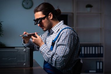 Genç erkek teknisyen geceleri atölyede bilgisayar tamir ediyor.