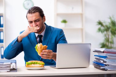 Genç erkek çalışan işyerinde kahvaltı yapıyor.