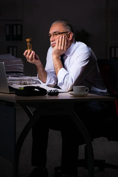 Oude mannelijke werknemer die laat op de werkplek werkt — Stockfoto