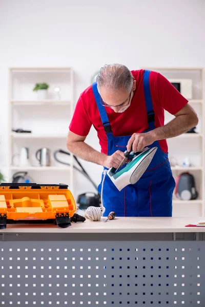 Velho empreiteiro masculino reparando ferro dentro de casa — Fotografia de Stock