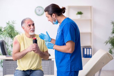 Yaralı yaşlı adam genç erkek doktor travmatoloğu ziyaret ediyor.