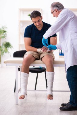 Genç yaralı adam yaşlı doktor travmatoloğu ziyaret ediyor.