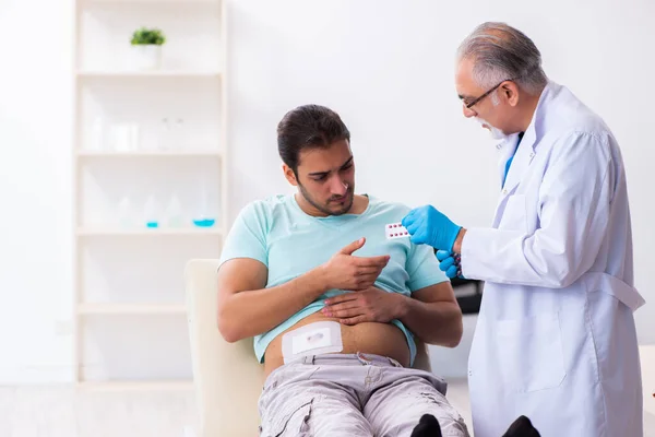 Yaralı genç adam deneyimli erkek doktoru ziyaret ediyor. — Stok fotoğraf