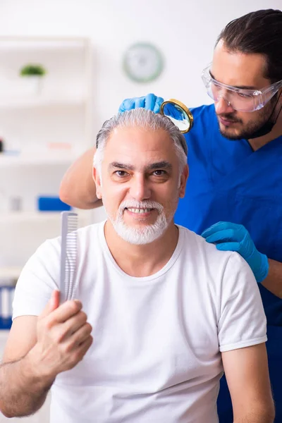 Old man visiting young male doctor in hair transplantation conce