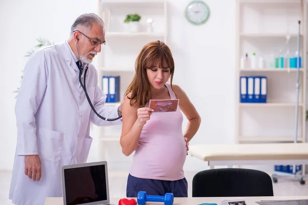 Jovem mulher grávida visitando velho médico ginecologista masculino — Fotografia de Stock