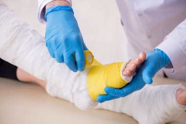 Genç bacak yaralı kadın yaşlı doktor travmatoloğu ziyaret ediyor.