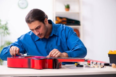 Gitarı tamir eden genç bir erkek tamirci.