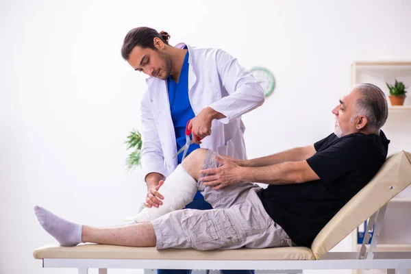 Viejo hombre herido visitando joven médico traumatólogo —  Fotos de Stock