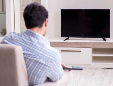 Genç adam evde televizyon izliyor.