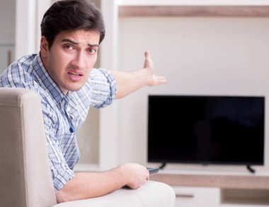 Genç adam evde televizyon izliyor.