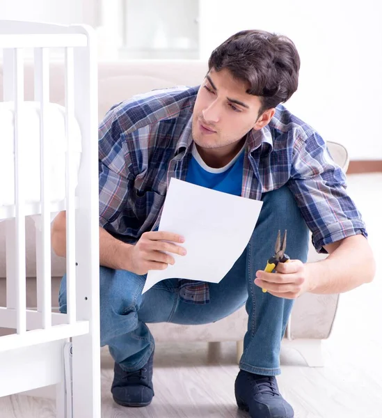 Jovem montando cama de bebê com manual de instruções — Fotografia de Stock