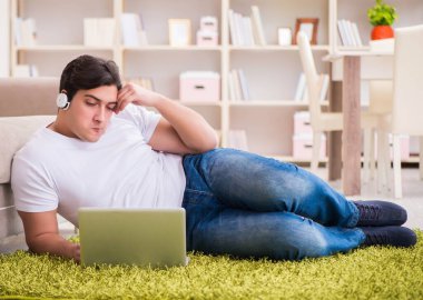 Evde, halı döşemesinde dizüstü bilgisayarda çalışan bir adam.