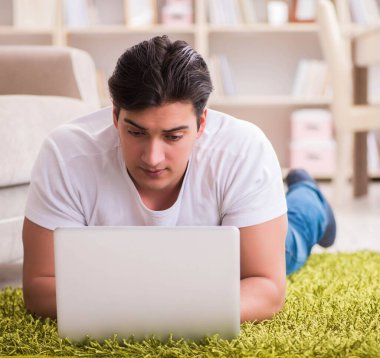 Evde, halı döşemesinde dizüstü bilgisayarda çalışan bir adam.