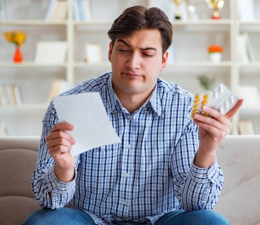 Kanepede ilaç ve reçeteyle oturan genç adam.